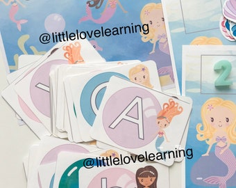 May include: A set of colourful alphabet flash cards featuring a mermaid and a letter on each card. The cards are designed for children learning their ABCs. The cards are on a blue background with a white border.