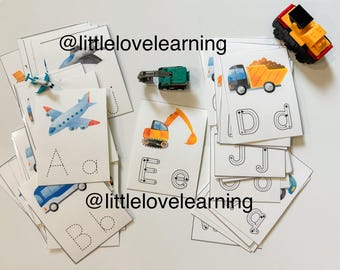May include: A set of flashcards featuring various vehicles and letters of the alphabet. The cards are white with black outlines and feature illustrations of a plane, a truck, a bulldozer, and a car. The letters are printed in black and are dotted for tracing. The text on the cards reads "@littlelovelearning".