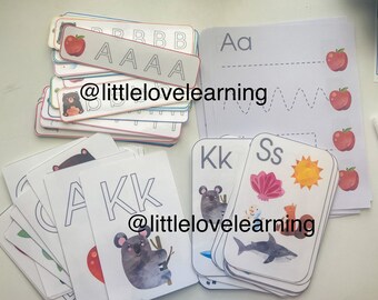 May include: A set of alphabet tracing cards featuring uppercase and lowercase letters, with illustrations of animals and objects. The cards are printed on white cardstock and have a colorful border. The cards are labeled with the letters "A", "K", "S", and "B". The cards also include the text "@littlelovelearning".