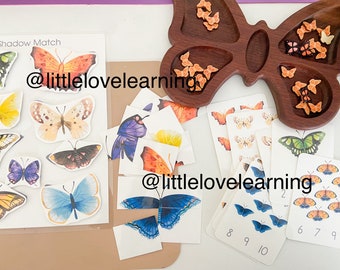 May include: A butterfly-shaped wooden tray with compartments filled with colourful butterfly-shaped counters.  There are also several cards with butterflies and numbers on them. The text "@littlelovelearning" is written on two of the cards.