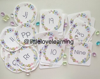 May include: A set of colourful floral-themed cards with letters and numbers. The cards are printed with a wreath of flowers and leaves. The letters include Jj, Pp, Ii, Rr, and G. The numbers include 19, 10, Nine, and Two. The cards are ideal for learning the alphabet and numbers.