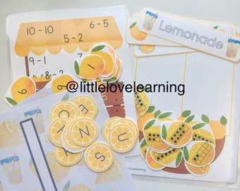 May include: A lemonade stand learning activity set with yellow and orange lemons, a brown wooden stand, and a sign that says "Lemonade". The set includes number cards, letter tiles, and ten-frames.
