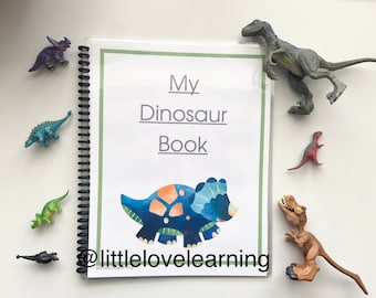 May include: A blue and green dinosaur book with the title "My Dinosaur Book" and the text "@littlelovelearning" on the cover. The book is surrounded by small plastic dinosaur toys.