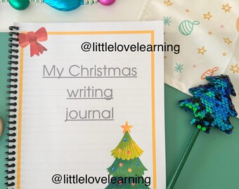 May include: A white journal with a yellow border and a Christmas tree illustration. The journal has the text "My Christmas writing journal" and the social media handle "@littlelovelearning" written on it.