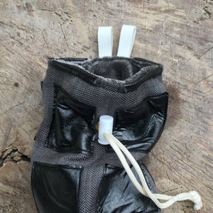 May include: A gray drawstring bag with black leather accents and a white drawstring. The bag has a white clip on the top and a white strap.