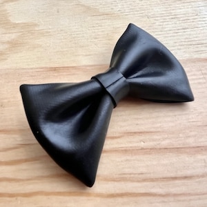May include: A black leather bow tie. The bow tie is tied and ready to wear.