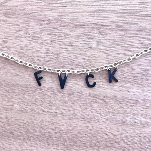 May include: A silver chain necklace with black letter charms spelling out the word "FVC".