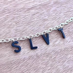 May include: A silver chain necklace with black letter charms spelling out the word "SLVT".