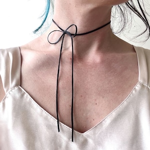 May include: A black choker necklace with a bow tie detail. The necklace is made of a thin, flexible material and has a simple, elegant design.