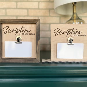 May include: Two wooden signs with the text "Scripture of the week" and a clip for holding a card. The signs are on a green table.