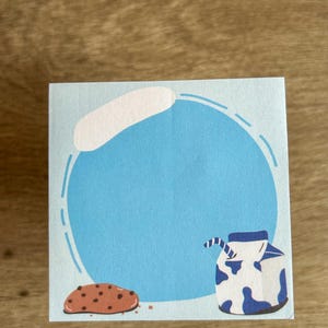 May include: A blue notecard with a white cloud and a blue circle with a brown cookie and a blue and white milk carton with a straw.