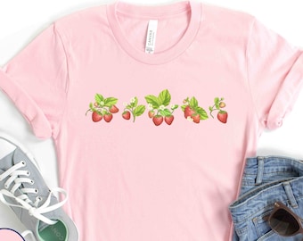 May include: Pink t-shirt with a row of strawberries printed on the front. The strawberries are red with green leaves and white flowers.
