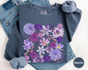 Könnte beinhalten: Ein dunkelblauer Pullover mit einem Blumendruck aus lila und weißen Blumen. Die Blumen sind in Bouquetform angeordnet und befinden sich mittig auf der Vorderseite des Pullovers.