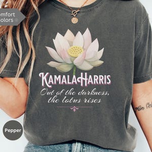 May include: A dark gray t-shirt with a pink lotus flower graphic and the text "KAMALA HARRIS Out of the darkness, the lotus rises".