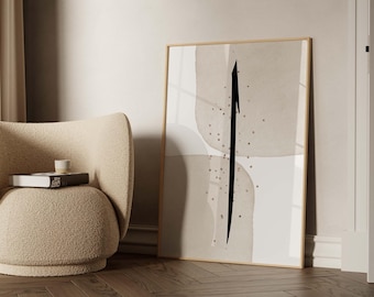May include: A framed abstract art print featuring a black arrow design on a neutral-toned background. The artwork is displayed in a light wooden frame, leaning against a wall. A beige armchair and a stack of books are in the foreground.