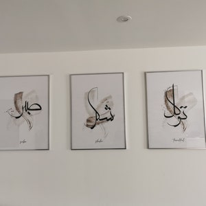 May include: Three framed prints with Arabic calligraphy in black ink on a white background. The prints are in silver frames and have the words "Jaber", "Shahe", and "Truthful" written below the calligraphy.