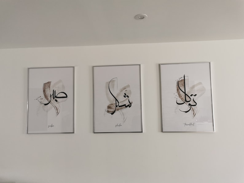 May include: Three framed prints with Arabic calligraphy in black ink on a white background. The prints are in silver frames and have the words "Jaber", "Shahe", and "Truthful" written below the calligraphy.