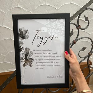 May include: A black framed print with a white background and a black and white floral design. The text "Teyzem" is written in cursive at the top of the print. The text below reads "Herzaman yanımızda ve arkamızda duran koca y&uuml;rekli kadın, herzaman iyiliğimizi isteyen, iyi niyetine inandığımız ve sonsuz g&uuml;vendiğimiz insan. Hem Anne yarısı, hemde canımızın yarısısın. Iyi ki varsın! Hayda, Emre & Solga"