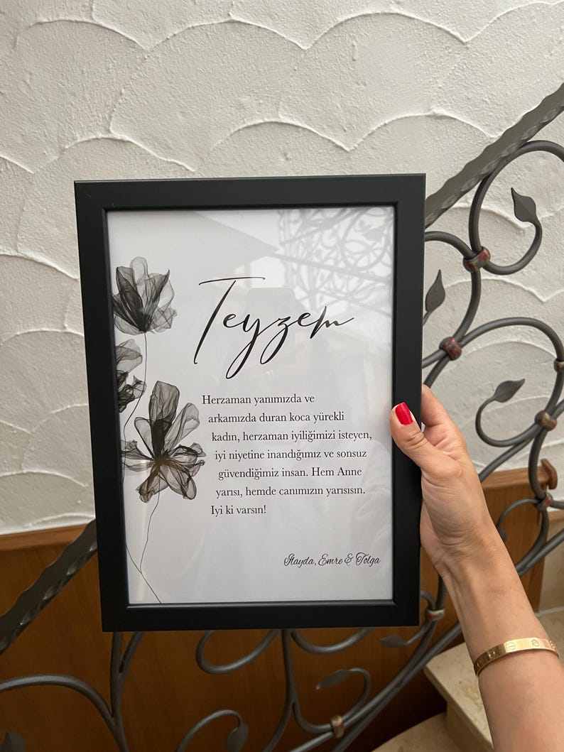 May include: A black framed print with a white background and a black and white floral design. The text "Teyzem" is written in cursive at the top of the print. The text below reads "Herzaman yanımızda ve arkamızda duran koca y&uuml;rekli kadın, herzaman iyiliğimizi isteyen, iyi niyetine inandığımız ve sonsuz g&uuml;vendiğimiz insan. Hem Anne yarısı, hemde canımızın yarısısın. Iyi ki varsın! Hayda, Emre & Solga"