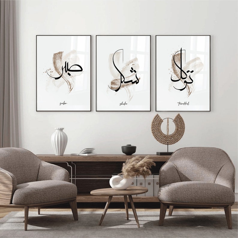 May include: Three framed prints with Arabic calligraphy in black ink on a white background. The prints are arranged in a row on a white wall. The words on the prints are "Sabr", "Shukr", and "Thankful".