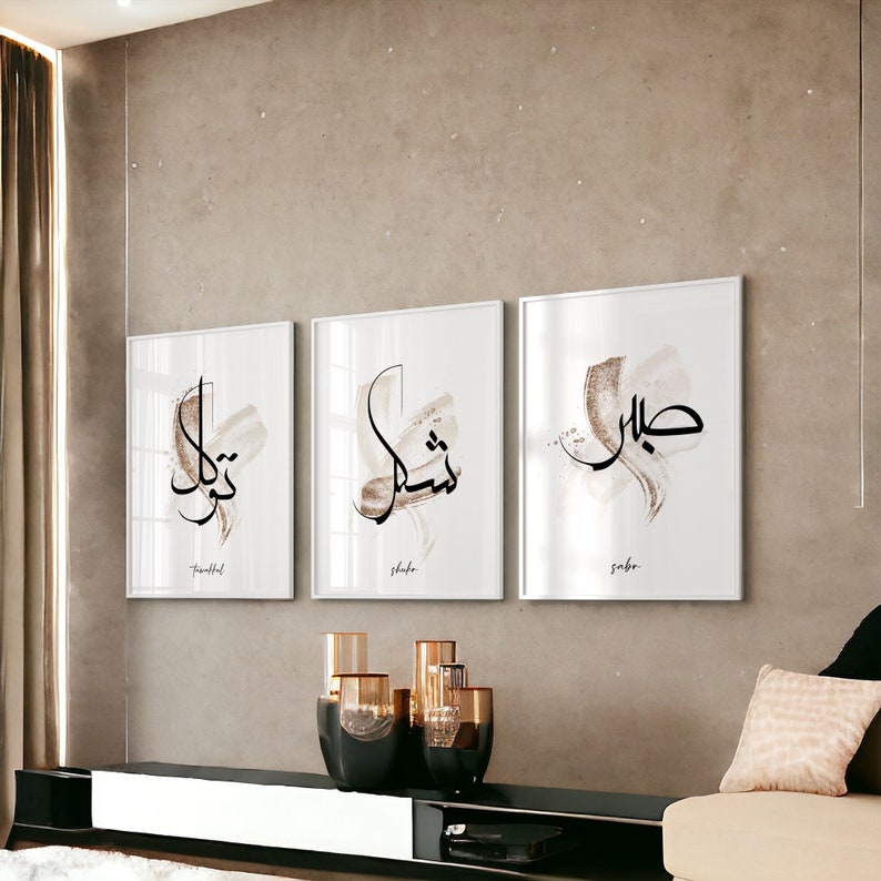 May include: Three framed prints with Arabic calligraphy in black ink on a white background. The prints are set against a light brown wall. The words on the prints are "Thankful", "Shukr", and "Sabr".
