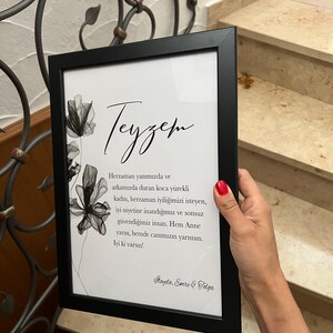 May include: A framed black and white print with a floral design and a handwritten message in Turkish that reads "Teyzem Herzaman yanımızda ve arkamızda duran koca y&uuml;rekli kadın, herzaman iyiliğimizi isteyen, iyi niyetine inandığımız ve sonsuz g&uuml;vendiğimiz insan. Hem Anne yarısı, hemde canımızın yarısısın. lyi ki varsın! Mayda, Emre & Tolga"