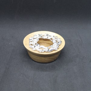 May include: A wooden candle holder with a silver decorative ring featuring a floral design.