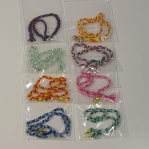 May include: Eight colourful braided cords with gold clasps, packaged individually in clear plastic bags. The cords are in various colours, including blue, red, yellow, green, and pink.