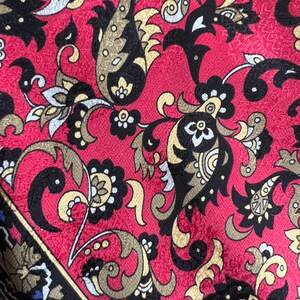 Puede incluir: Una tela con un fondo rojo vibrante y un patr&oacute;n repetitivo intrincado de motivos de cachemira y elementos florales estilizados en negro, dorado y blanco. El dise&ntilde;o incluye enredaderas y formas detalladas en la superficie.