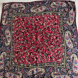 Puede incluir: Un pa&ntilde;uelo cuadrado con un panel central rojo con un denso patr&oacute;n floral negro y dorado, rodeado por un borde negro con grandes motivos de cachemira coloridos en tonos azul, amarillo y rojo. El texto Laura Biagiotti es visible.
