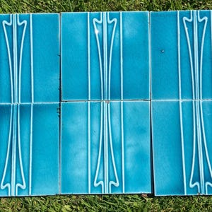 Peut inclure: Ensemble de six carreaux de céramique turquoise avec un motif floral blanc stylisé. Les carreaux sont disposés en deux rangées de trois, le motif étant vertical. Les carreaux sont posés sur de l'herbe.