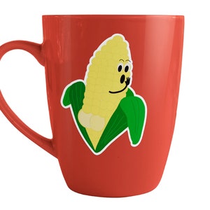 Könnte beinhalten: Eine rote Keramiktasse mit einem Cartoon-Mais-Design. Der Maiskolben hat ein lächelndes Gesicht und trägt eine grüne Hülle.