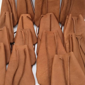 Peut inclure: Plusieurs pochettes en cuir marron avec cordon de serrage, de tailles variées. Chaque pochette a un fond arrondi et une fermeture à cordon en haut. Le cuir présente un aspect texturé, et les pochettes sont rapprochées.