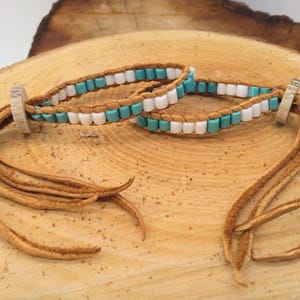 May include: Two leather bracelets with turquoise and white beads. The bracelets have brown leather tassels.