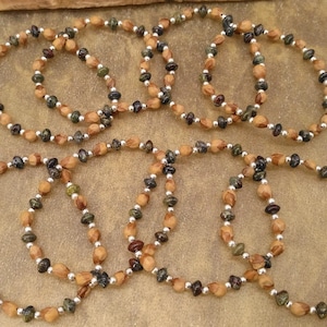May include: A collection of beaded bracelets. The bracelets are made with light brown, dark green, and dark brown beads, with small silver-coloured beads. They are displayed on a textured, tan surface.