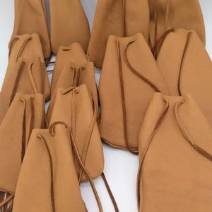 Pode incluir: Uma coleção de bolsas de couro castanho-claro com fechos de cordão. As bolsas variam em tamanho e forma, com um design simples e rústico. O couro parece macio e flexível, com um grão natural. Os cordões são castanho-escuro.