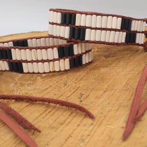 Puede incluir: Dos pulseras de cuero con cuentas blancas y negras y borlas de cuero marrón.