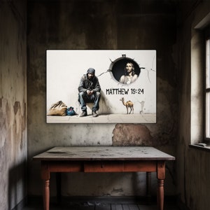 May include: A white canvas print with a black and white image of a man sitting on a sidewalk with a camel and a figure of Jesus in a hole in the wall. The text "MATTHEW 19:24" is written on the wall.
