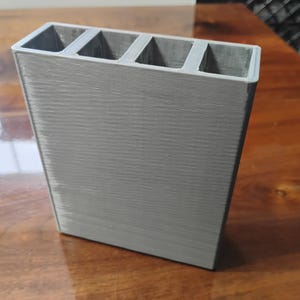 May include: A gray plastic organizer with five compartments. The organizer is designed to hold small items, such as pens, pencils, or other office supplies.