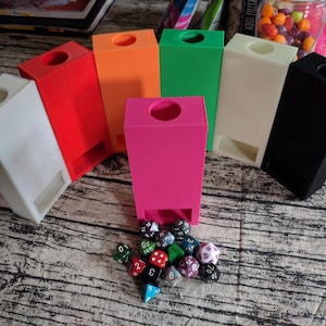 May include: A set of ten colourful dice towers, made of plastic, in various colours including white, red, orange, green, and black. The towers are arranged in a semi-circle on a wooden surface. A collection of colourful dice are scattered in front of the towers.