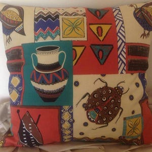 Könnte beinhalten: Quadratisches Zierkissen mit Patchwork-Design. Das Kissen zeigt verschiedene geometrische Formen, darunter Dreiecke und Quadrate, sowie Illustrationen von Vögeln, Insekten und Vasen. Die Farbpalette umfasst Rot, Blau, Gelb und Teal.