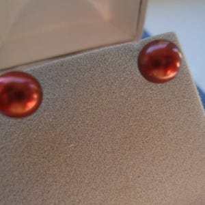 May include: A pair of red pearl earrings in a small, beige jewelry box.