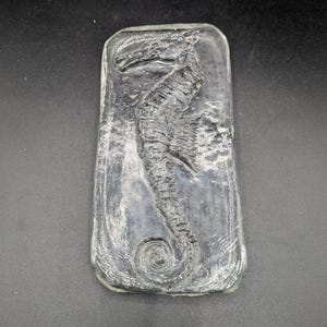 May include: A clear, rectangular glass piece with a seahorse design. The seahorse is raised and detailed, with a curled tail. The glass has a slightly textured surface, and the seahorse is centered within the rectangle.