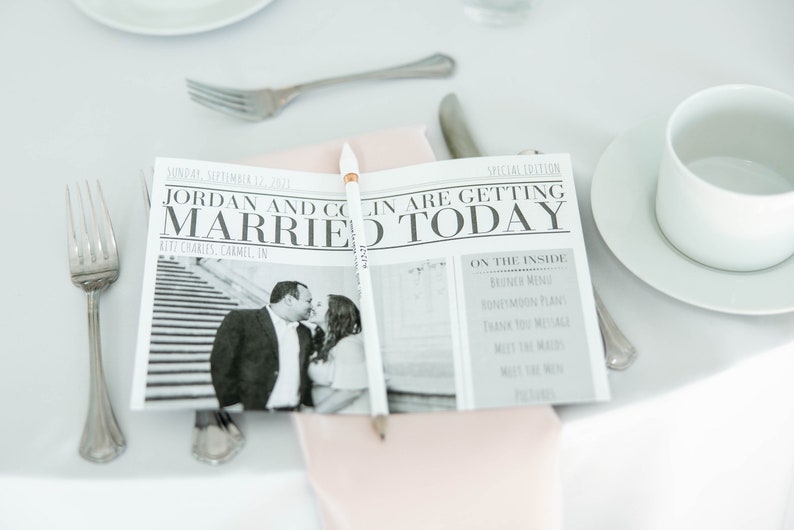 Puede incluir: Un peri&oacute;dico de boda con el titular "Jordan and Colin Are Getting Married Today" se muestra sobre un mantel blanco. El peri&oacute;dico incluye una foto en blanco y negro de la pareja y un l&aacute;piz. Tambi&eacute;n se ven cubiertos y una taza de t&eacute; blanca.