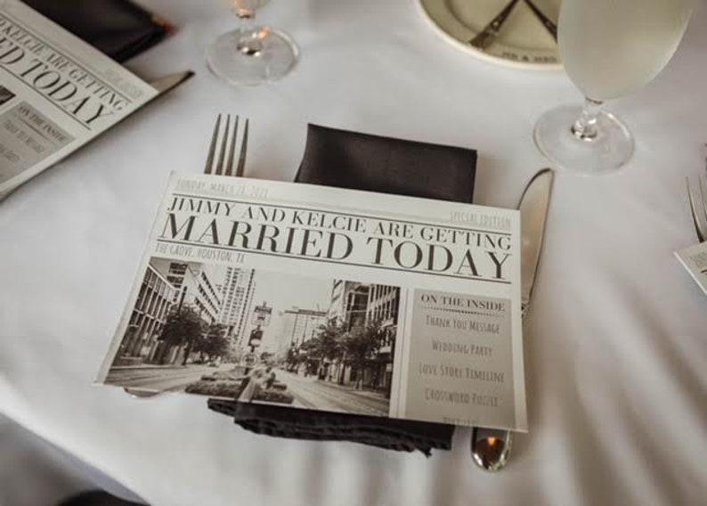 Puede incluir: Un anuncio de boda en blanco y negro dise&ntilde;ado como un peri&oacute;dico. El titular dice "Jimmy and Kelcie are getting Married Today". El anuncio incluye una foto de una calle de la ciudad.