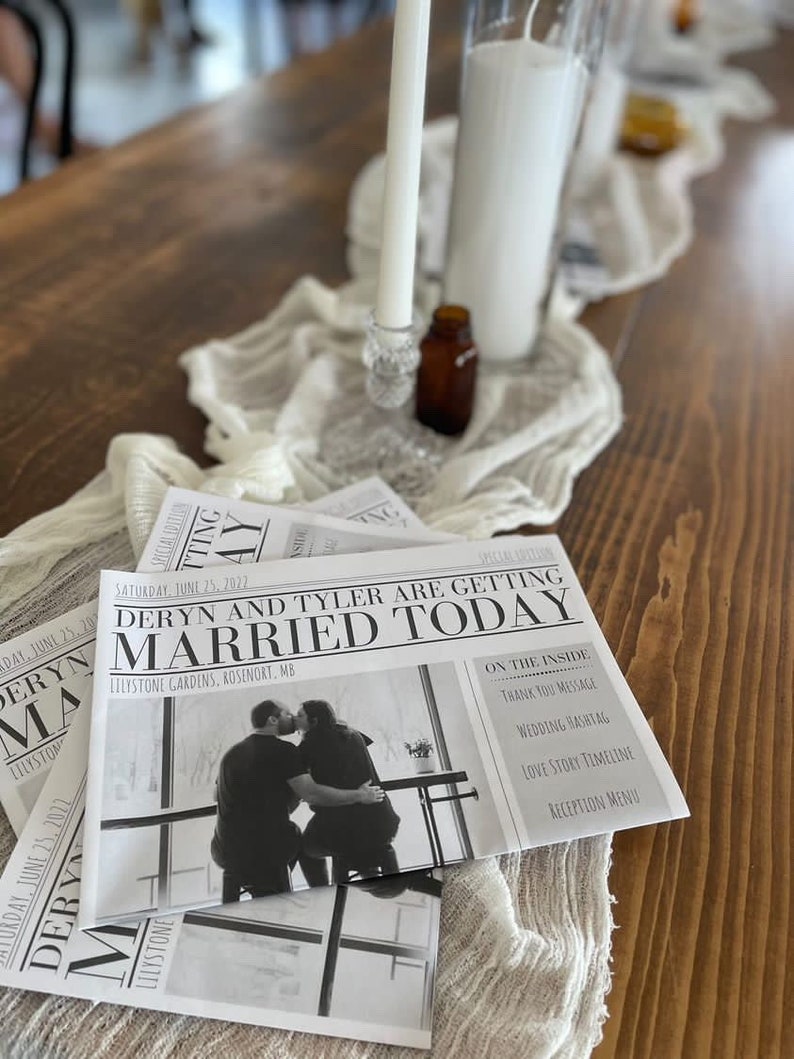 Puede incluir: Programas de boda con dise&ntilde;o de peri&oacute;dico, con el titular "Deryn and Tyler are getting married today" y una foto de la pareja. Est&aacute;n sobre una mesa de madera con un camino de mesa blanco, velas y una peque&ntilde;a botella marr&oacute;n.