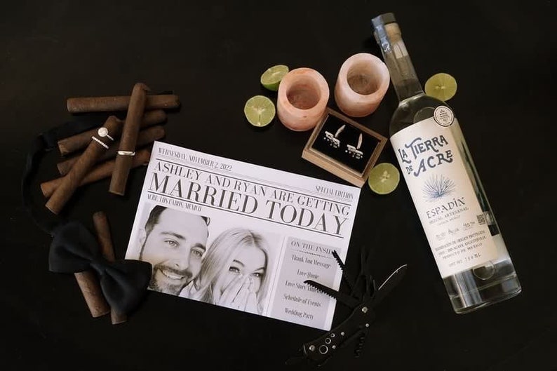Puede incluir: Una composici&oacute;n tem&aacute;tica de boda con cigarros, anillos, una pajarita y un peri&oacute;dico con el titular "CASADOS HOY". Tambi&eacute;n incluye una botella de tequila, gajos de lima y una multiherramienta, todo sobre una superficie negra.