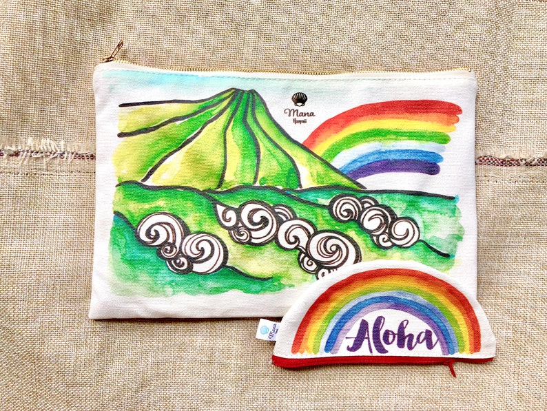 May include: A white canvas zippered pouch with a watercolour illustration of a green mountain with a rainbow arching over it. The pouch has a smaller matching rainbow pouch with the word "Aloha" written in purple on it.