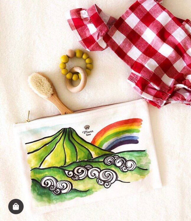 May include: White zippered pouch with a watercolour illustration of a green mountain, rainbow, and clouds. The text "Mana Hawaii" is printed on the pouch.