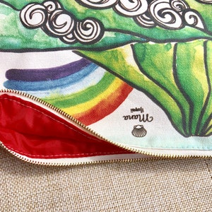 May include: A white canvas zippered pouch with a colourful rainbow design and green leaves with swirls. The pouch is lined with red fabric and has a small shell logo that says "little mermaid".